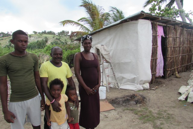 Christophe and his family in front of their current home. They are trying to build a concrete block home to live in which JUST MERCY is helping with.